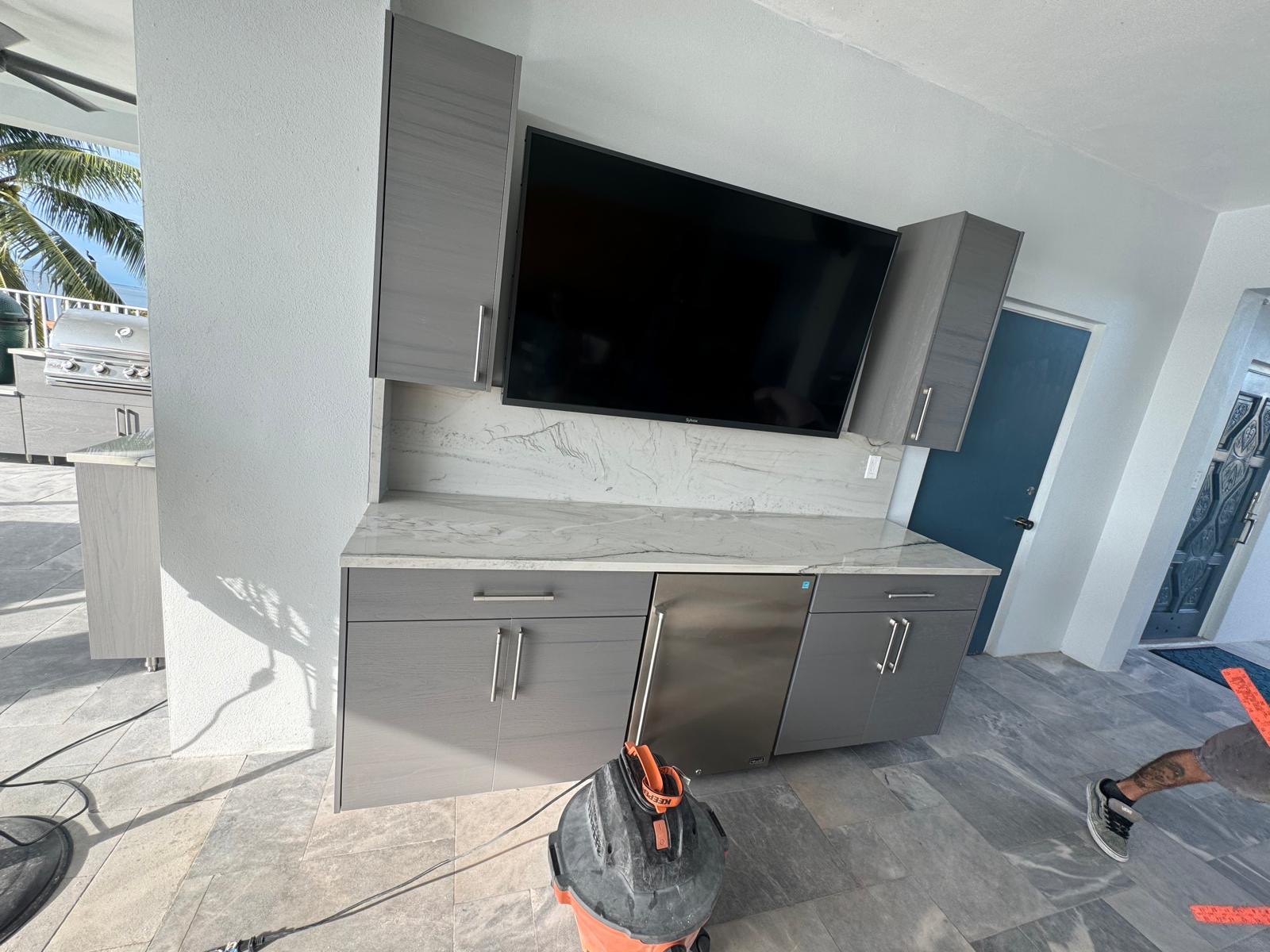 Outdoor kitchen installation with gray cabinets, a stone-look countertop and an under-counter refrigerator