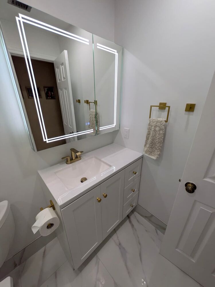 White vanity with an illuminated mirror and brushed gold fixtures in the completed Kendall bathroom