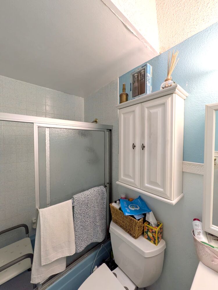 Old framed shower door with towels, vanity cabinet and over-toilet cabinet